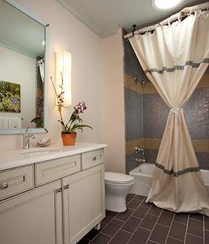 Bathroom with cream painted vanity, mosaic tile shower, and warm accent lighting.
