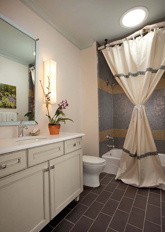 Bathroom with cream painted vanity, mosaic tile shower, and warm accent lighting.